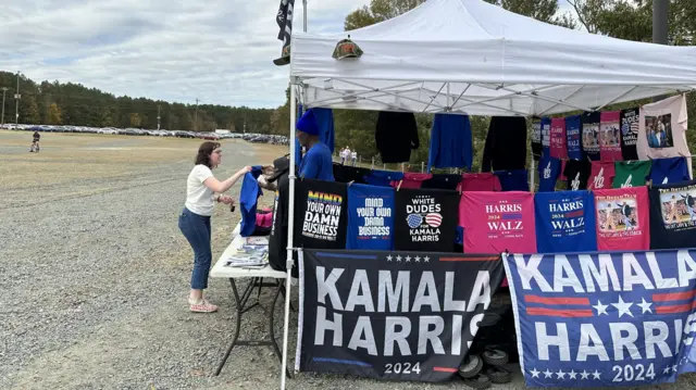 A woman buying merchandise from a stand selling Kamala Harris 2024 flags and t-shirts