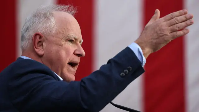 Tim Walz gestures as he campaigns in Arizona against the backdrop of an American flag