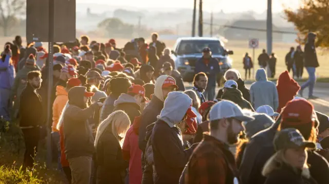 A long queue of people, with many wearing red MAGA hats