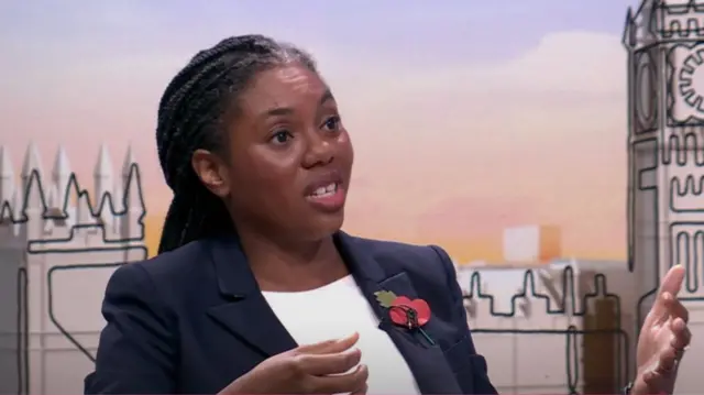 Kemi Badenoch speaks, her hands both raised in front of her with left palm open, right palm slightly pulled closer to her chest