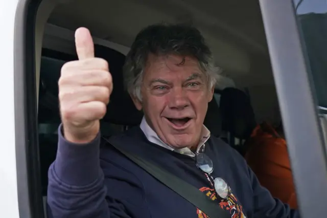 A man gives a thumbs-up gesture out the window of a car.