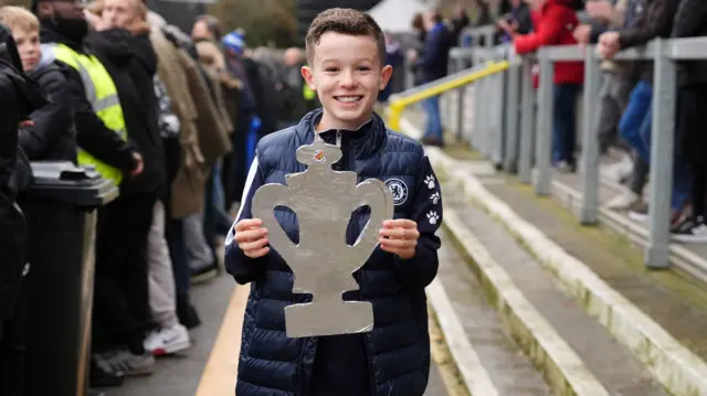 A young fan at Wealdstone's Grosvenor Vale ground holds a tinfoil FA Cup trophy