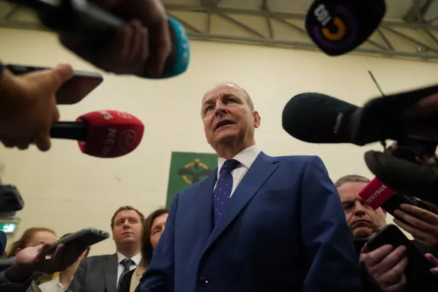 Micheál Martin, a man in a navy suit, surrounded by media.