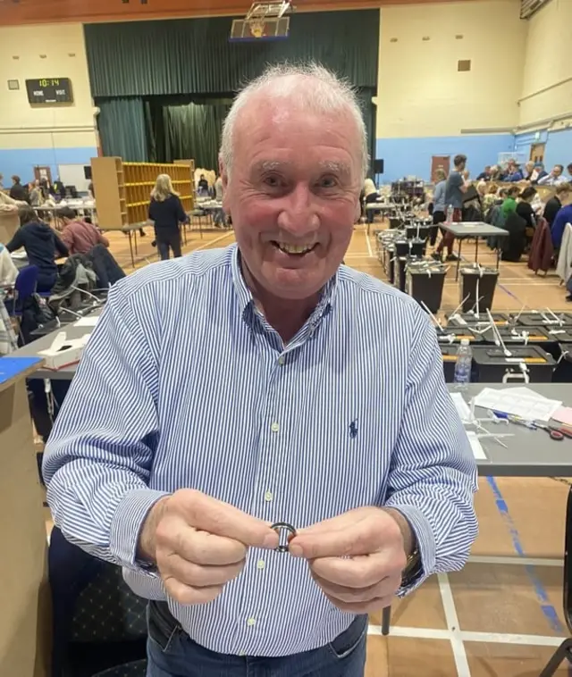 Counter Peter Creamer holding the ring, he is wearing a blue and white striped shirt