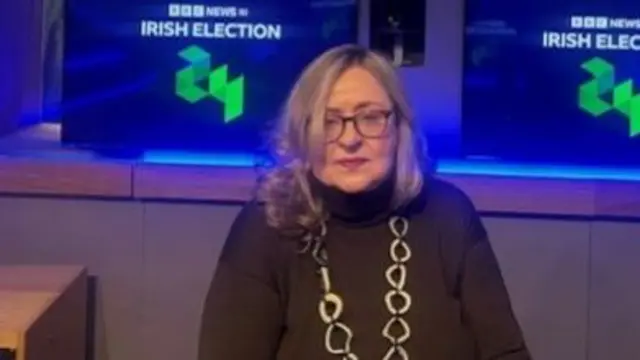 Woman sits in front of a graphic which says BBC News NI Irish Election