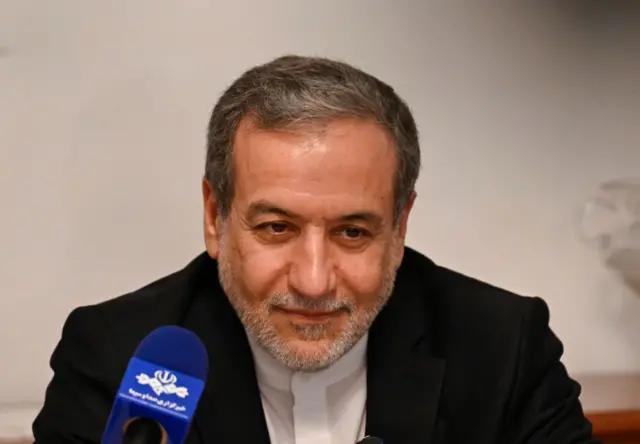 Headshot of  Abbas Araghchi smiling in front of a microphone