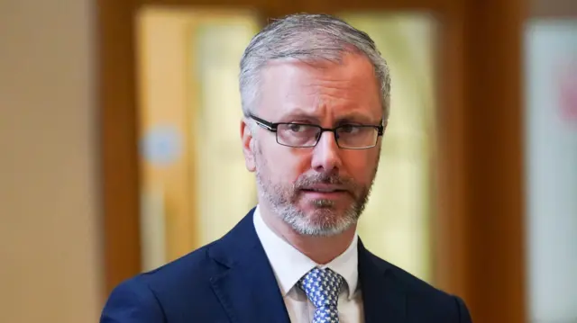 Roderic O'Gorman, a man with grey hair and a tight grey beard. He is wearing a navy suit and glasses.