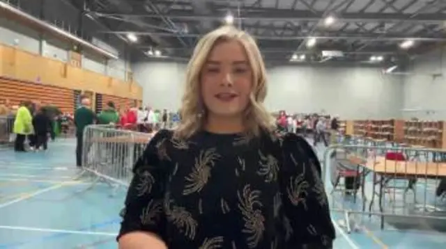 A woman wearing a black top speaks in a leisure centre.