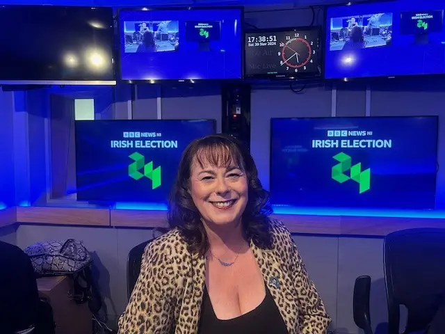 A woman in a leopard-print jacket sits on front of a graphic saying BBC News NI Irish Election