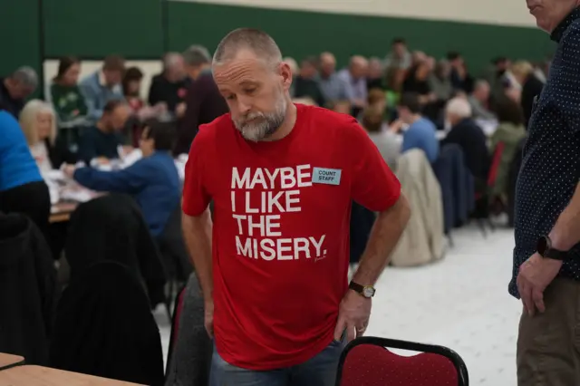 A man in a red t-shirt which says 'maybe I like the misery'