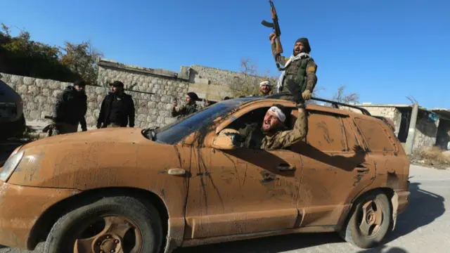 Anti-government fighters seen raising their arms and a gun from inside a car