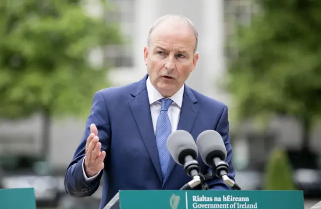 A man makes a speech with a lectern saying Government of Ireland in front of him.