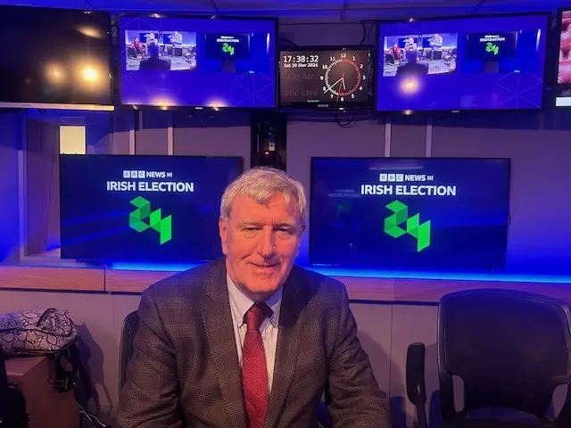 A man wearing a suit sits in front of a graphic saying BBC News NI Irish Election