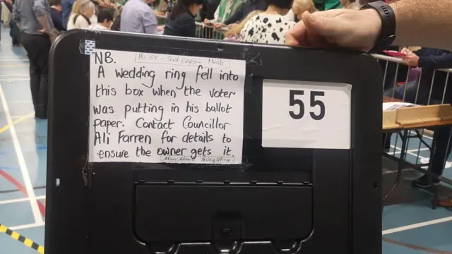 A note that on a black lid that says NB. A wedding ring fell into this box when the voter was putting in his ballot paper. Contact councillor Ali Farren for details to ensure the owner gets it.