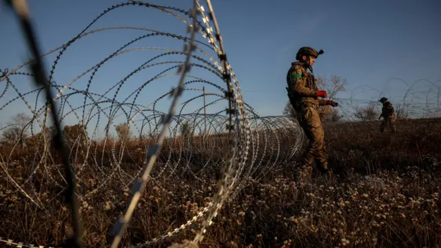 A Ukrainian soldier leans against some barbed wire