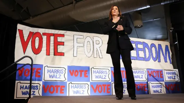 Kamala Harris poses in a black suit in front of a sign that says Vote For Freedom.