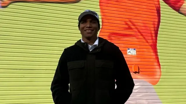 Roger Salazar poses for a photo in a car park beside a brightly-pained building