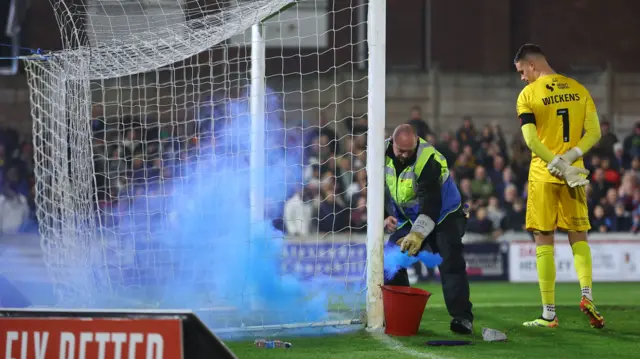 Play is stopped as a flare is removed from the Lincoln City goalmouth