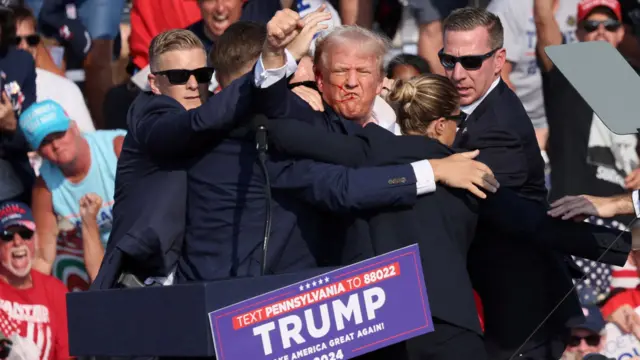 Surrounded by security personnel, Donald Trump gestures with a bloodied face during a campaign rally