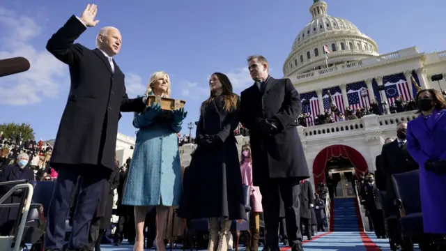 Joe Biden raises his hand with the other on a bible as he's sworn in as president in 2021, standing beside his wife Jill Biden