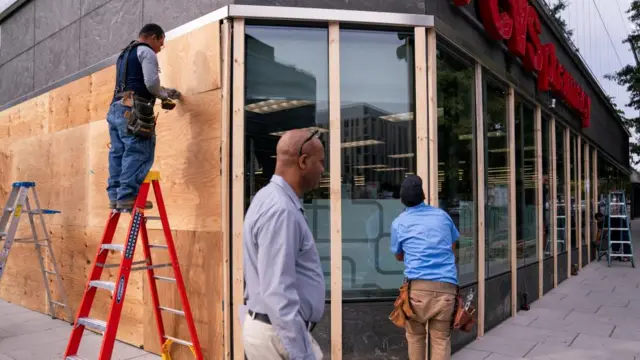 Workers cover the windows of a pharmacy near the White House with plywood