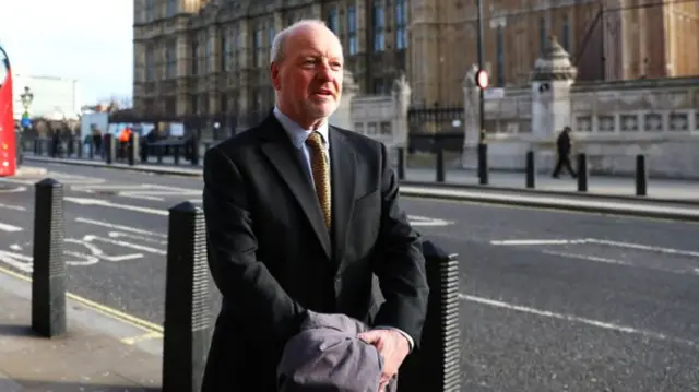 Sir Alan Bates wears a suit in front of House of Commons