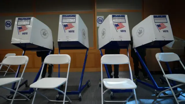 Four white voting booths with chairs in front of them