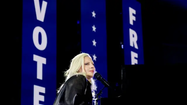 Lady Gaga sings at a piano against a backdrop reading 'Freedom Vote'