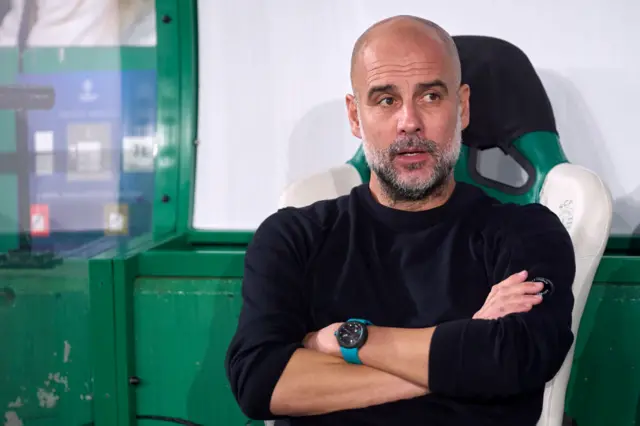 Guardiola sits in his seat on the bench with arms crossed