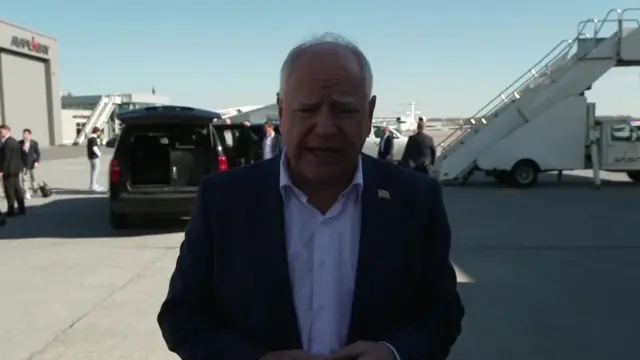 Walz speaks on the tarmac next to a plane