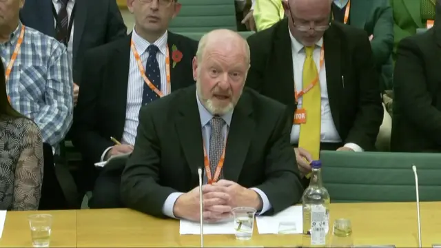 Sir Alan Bates sits at a table at the business select committee, with his hands clasped together, as he gives evidence to MPs