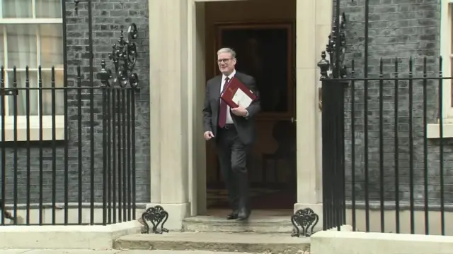 Starmer holding a red book, walking out the door of No 10 Downing Street