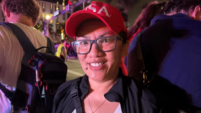 A woman in glasses and a red 'USA' cap smiles for the camera