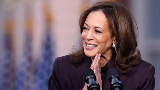 Kamala Harris clasps her hands while standing at a lectern