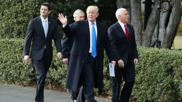 Donald Trump, wearing a black coat over a white shirt and blue tie, waves as he walks through the White House lawn with Mike Pence, Paul Ryan and Mitch McConnell, all wearing suits and ties