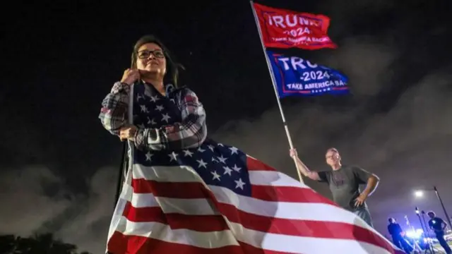 A woman, shrouded in the American flag, looks on