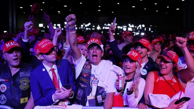 A line of supporters, all wearing red caps, cheer with one man raising his fist in the air