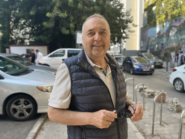 Omar Baalbahi standing in a street wearing a grey T-shirt and black puffer jacket