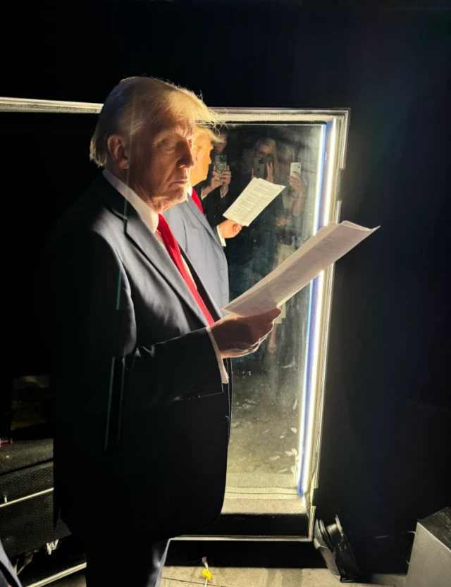 Donald Trump next to a mirror holding paper