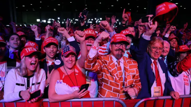 Trump supporters raise their fists and cheer while waiting to see him on stage