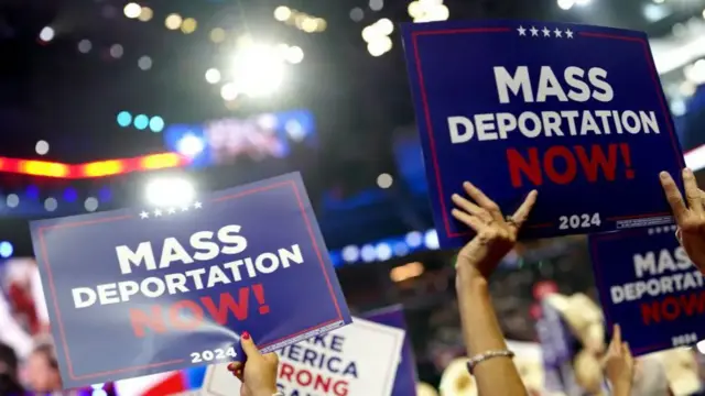 People holding signs saying 'mass deportation now' at a Trump event