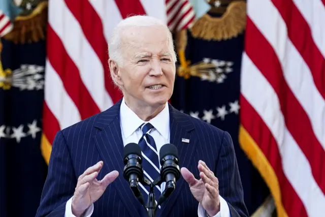 Joe Biden gestures at a lectern in front of American flags