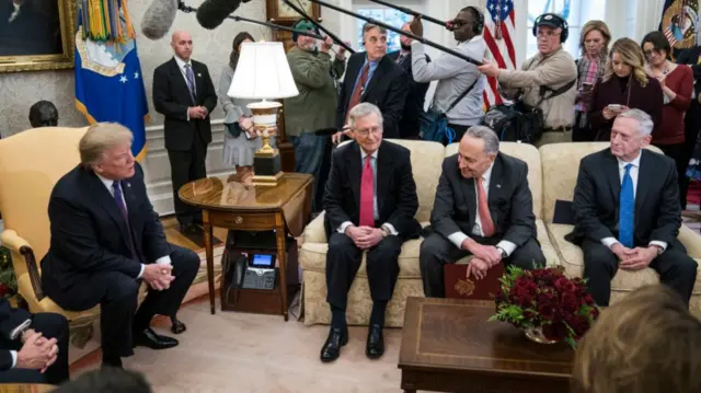 Trump sits in the Oval Office with congressional leaders surrounded by members of the media