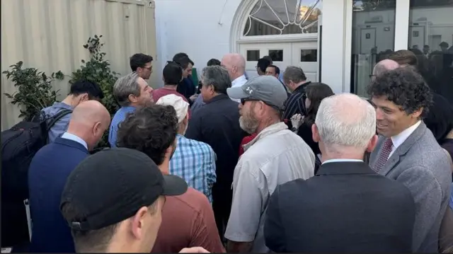 Group of reporters wait in the Rose Garden for Joe Biden's speech. The group is just outside a white door