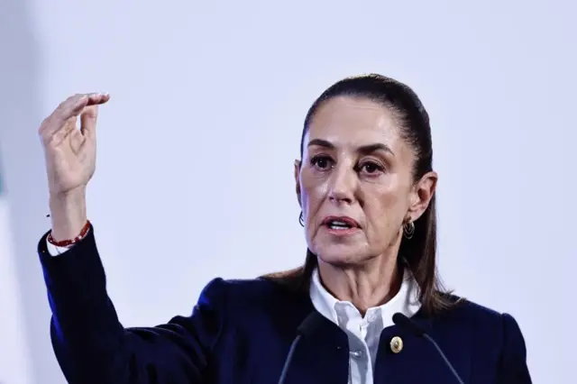 Claudia Sheinbaum speaking into two microphones and holding one hand in the air