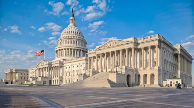 Exterior shot of US Congress taken from the right. US flag flying in front of central dome