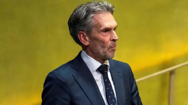 Dutch PM Dick Schoof stands before a yellow backdrop