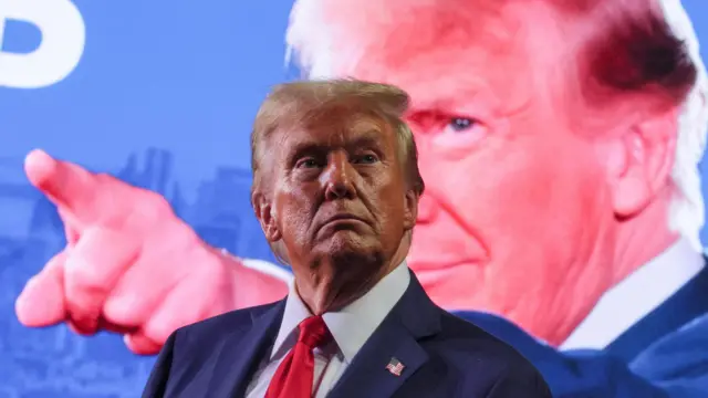 Trump standing in front of a billboard of him pointing