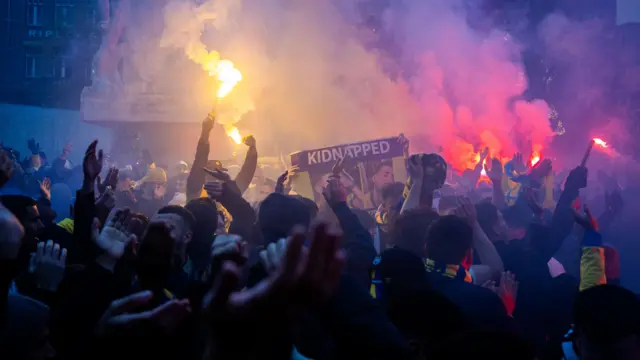 Maccabi Tel Aviv supporters gather at the Dam square, with one holding a "Kidnapped" sign and several flares lit