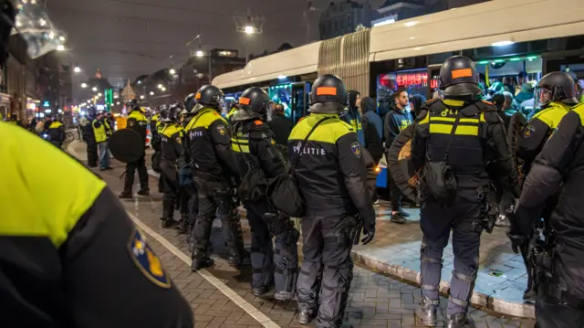 Line of police officers standing in front of a bus with football fans inside